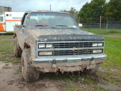 1991 Chevrolet Blazer - A heavily mud-splattered Chevrolet pickup truck is parked on a dirt road, with an ambulance visible behind it.