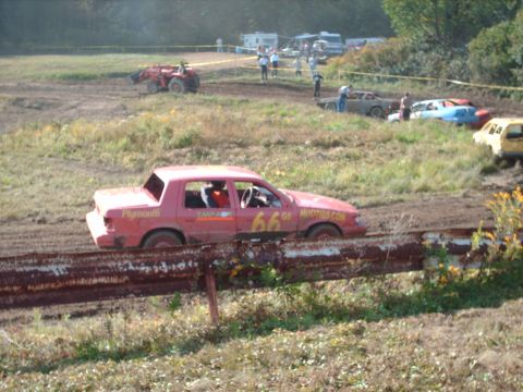 1991 Chevrolet Blazer - Demolition derby cars are stuck in the mud during an event, with spectators and other vehicles in the background.