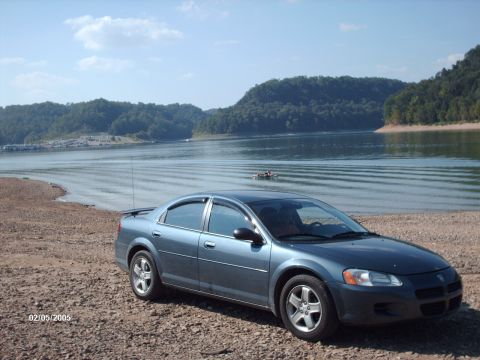 1995 Ford Probe - A blue sedan sits on a rocky shore beside a calm lake under a partly cloudy sky.