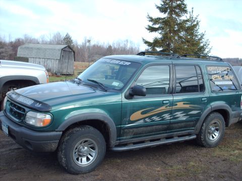 1991 Chevrolet Blazer - A green SUV with 'EXPLORER' on the windshield and 'HOFFY'S GRAPHICS' on the rear window is parked next to a silver truck.