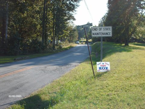 1995 Ford Probe - A white sedan is seen on a rural road near signs for 'Cave Springs' and 'End of State Maintenance'.