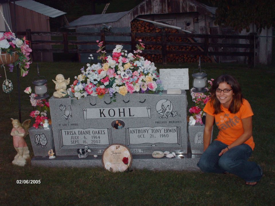 Woman kneeling by a gravestone with flowers and names