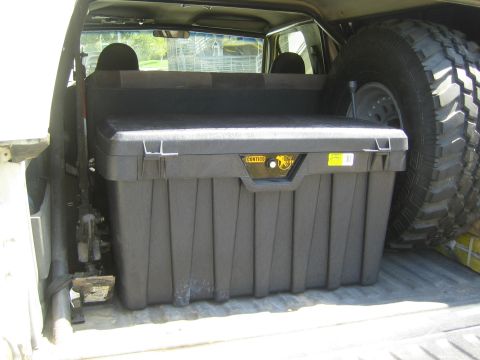 1990 Ford Bronco - black Contico storage chest sits in a pickup truck bed next to a large spare off-road tire.