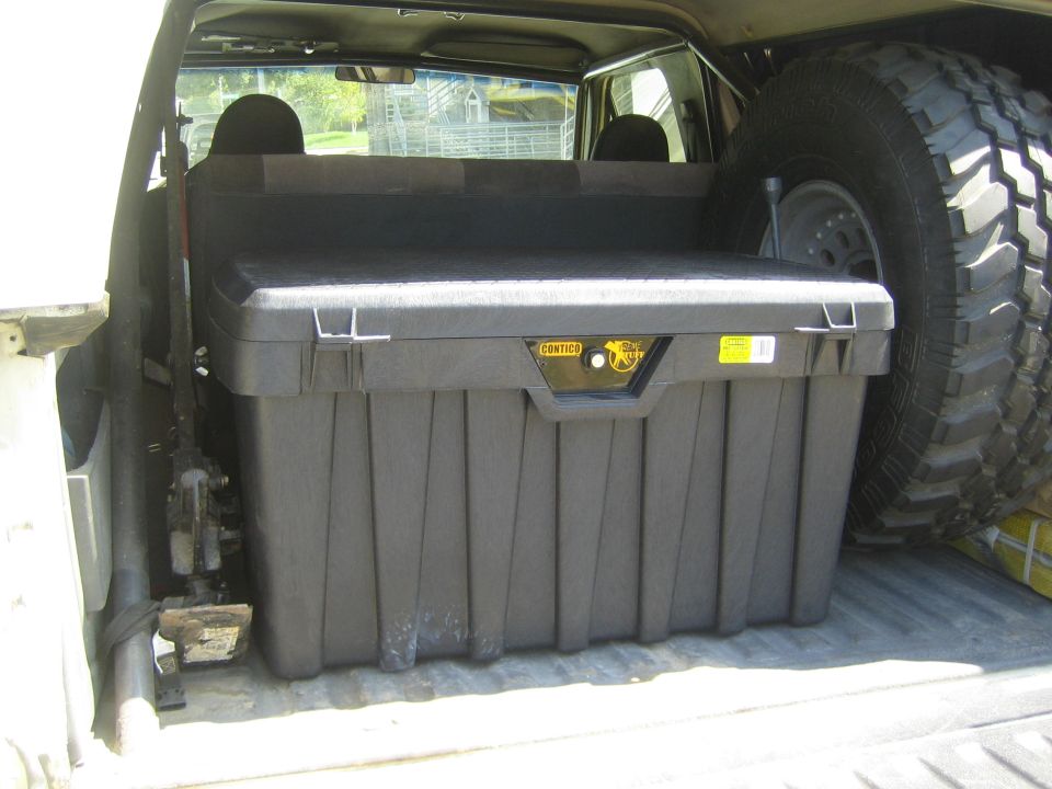 Black Contico storage box in the bed of a pickup beside a spare off-road tire