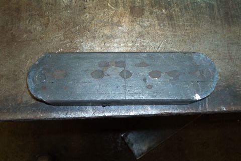 1983 Ford Bronco - A metal part with rounded ends and center line marking is shown on a workbench.