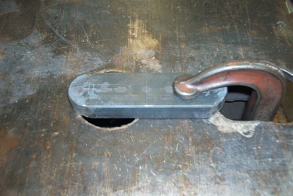 Metal plate with rounded ends held by a C-clamp on a workbench