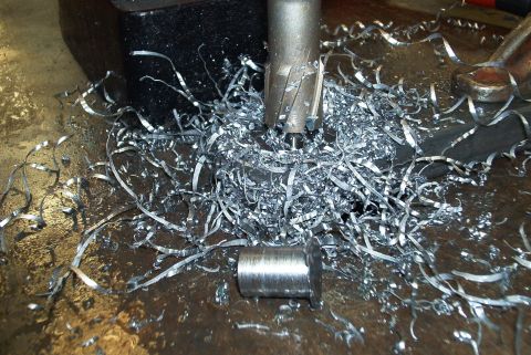 1983 Ford Bronco - Metal shavings and a machined part are visible on a workbench with a drill bit overhead.
