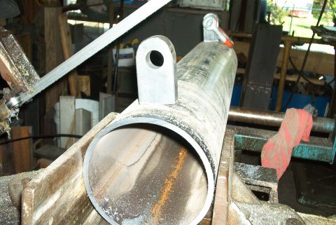 1983 Ford Bronco - A metal pipe is being cut by a bandsaw in a workshop setting.