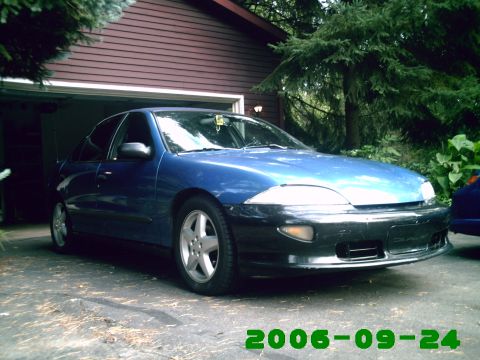 1996 Chevrolet Cavalier - A blue sedan with a black front bumper and aftermarket wheels sits in front of a garage.