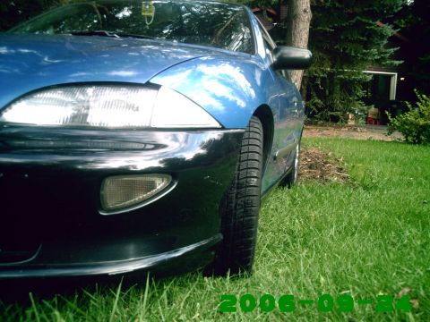 1996 Chevrolet Cavalier - The front corner of a blue sedan is shown parked on a grassy lawn next to a house.