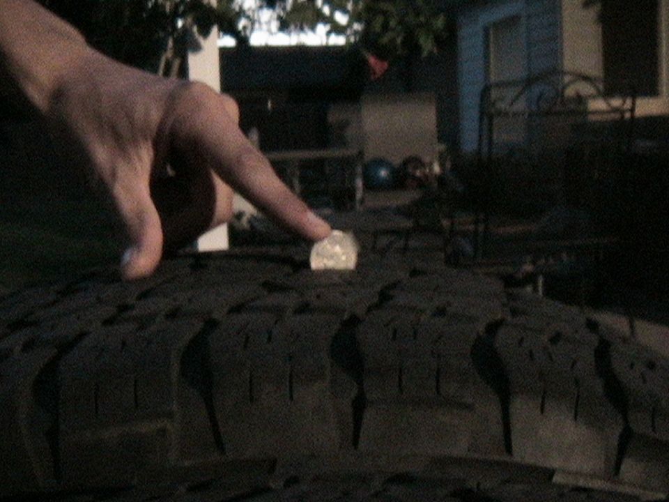 Finger pointing at a coin on a tire tread to show depth