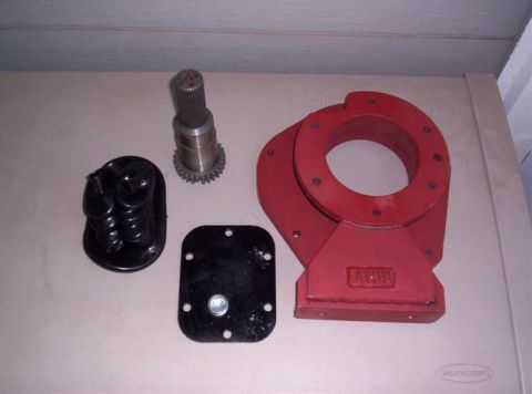 1995 Ford Bronco - A collection of automotive parts, including a red housing and a splined shaft, are displayed on a flat surface.