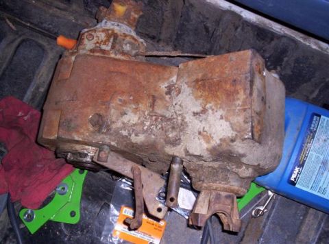 1995 Ford Bronco - A heavily rusted transfer case, likely for a 1995 Ford Bronco, sits next to a blue fluid bottle and red cloth.