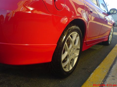 2005 Dodge SRT-4 - Close-up of a red sedan's rear wheel and lower body panel parked next to a yellow curb.