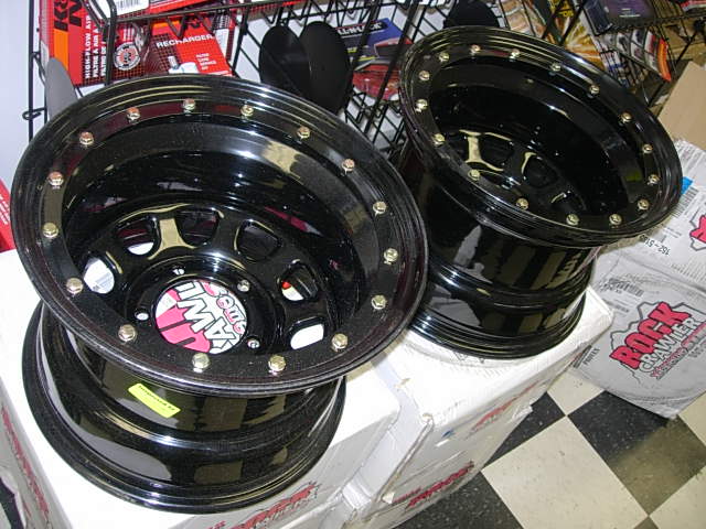 Two black off-road wheels with red and white center caps. Boxes labeled "Rock Crawler" are in the background
