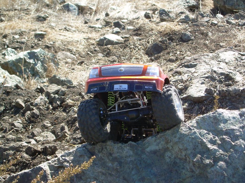 Red RC Cadillac Escalade crawler perched on a rock, front view