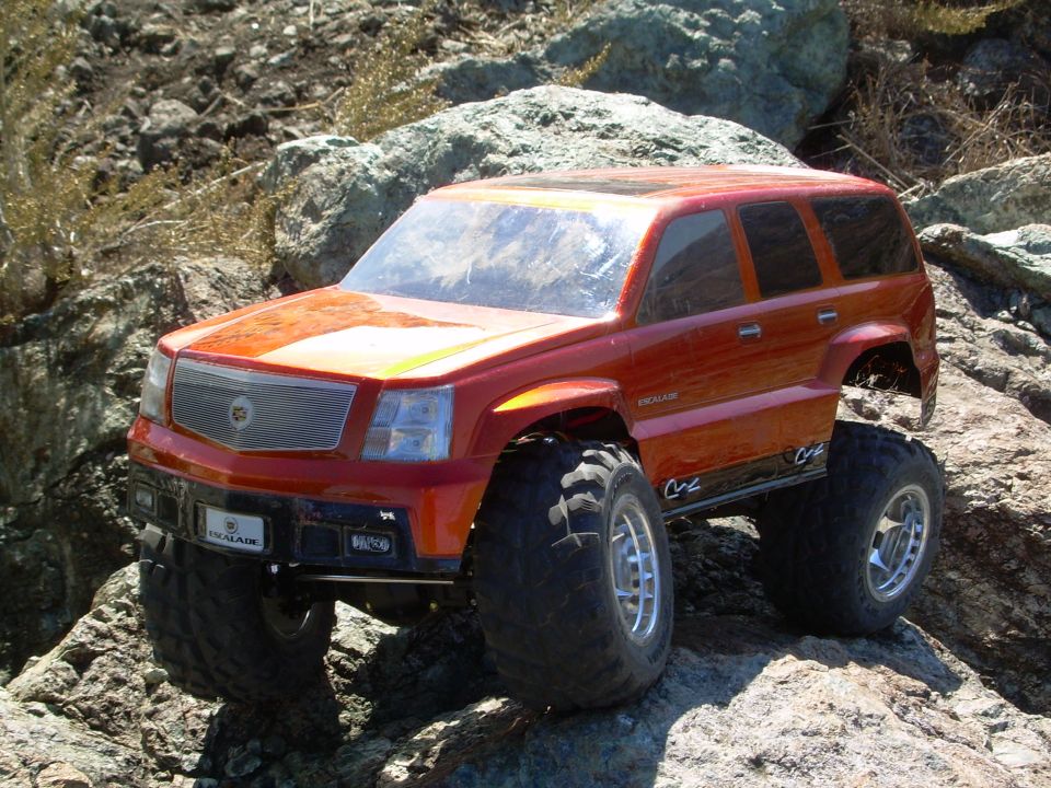 Orange RC Cadillac Escalade crawler on rocks, front three-quarter