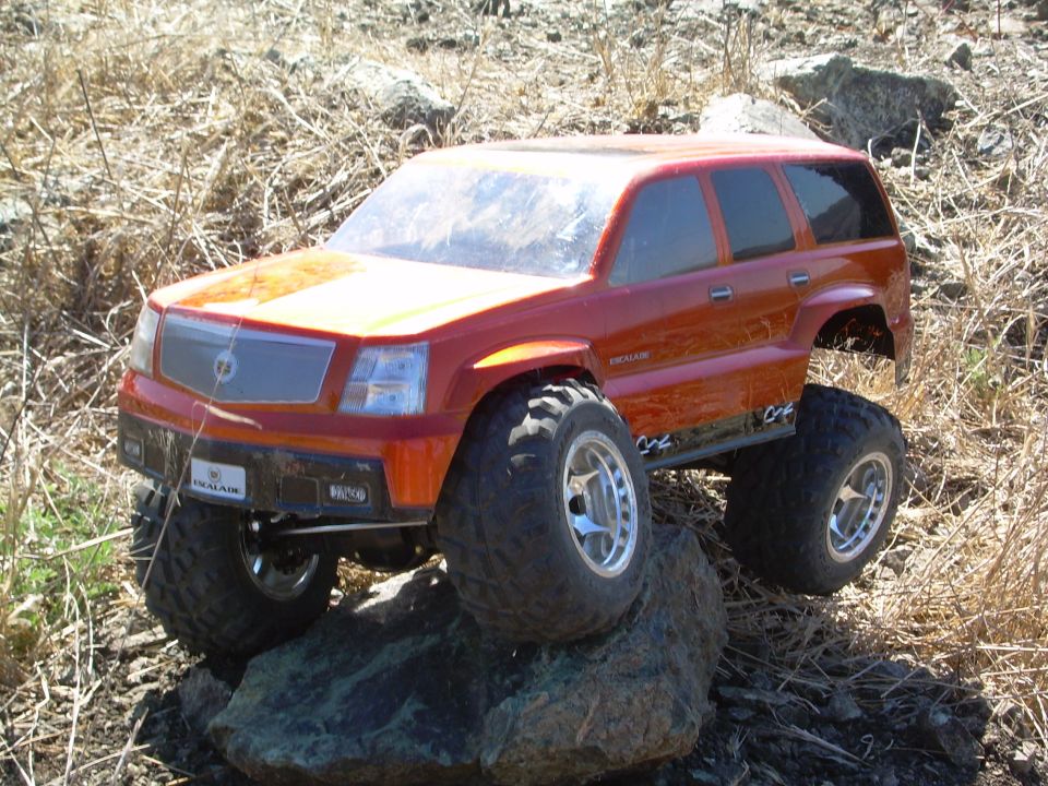 Orange RC Cadillac Escalade crawler atop a rock in dry brush