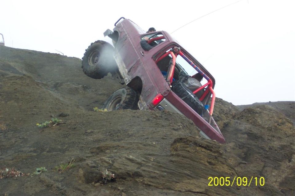 Maroon Ford Bronco with roll cage climbing steep rocky hill at near-vertical angle