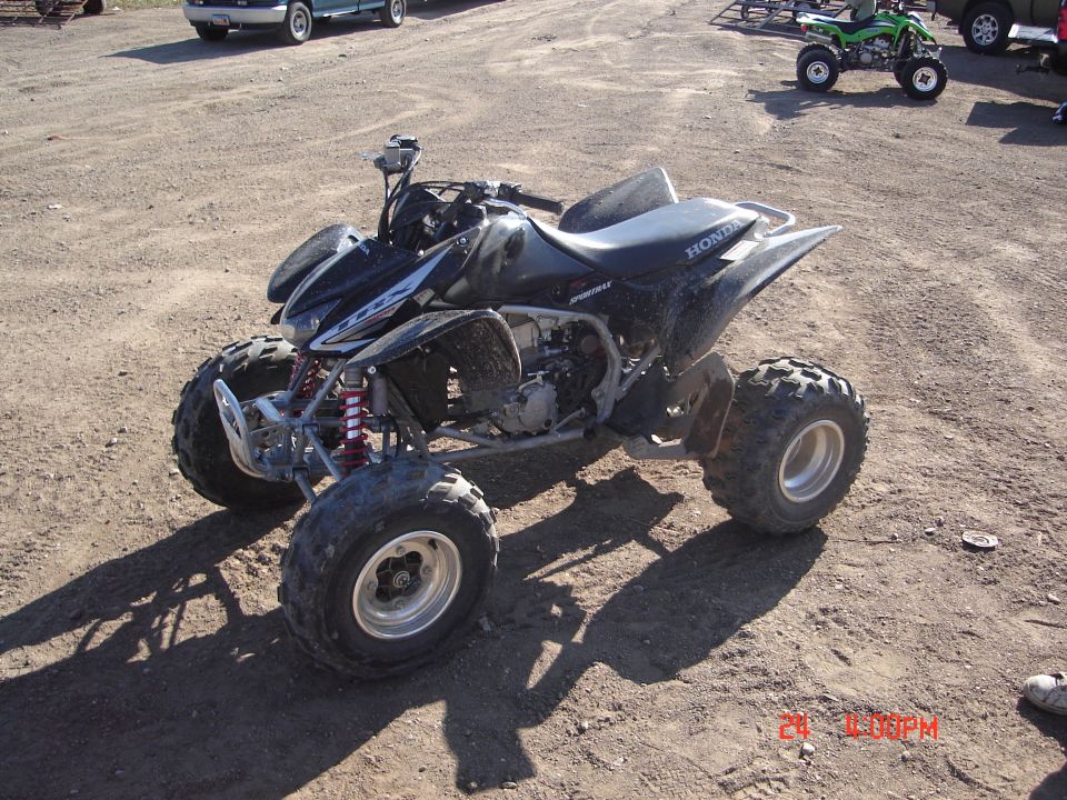 Black Honda sport quad ATV parked on dirt with other quads behind