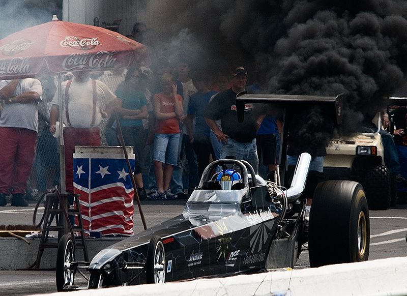 Black and silver rail dragster on the starting line amid heavy black smoke