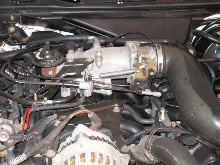 Installed V8 throttle body with linkage, return spring and cables in engine bay