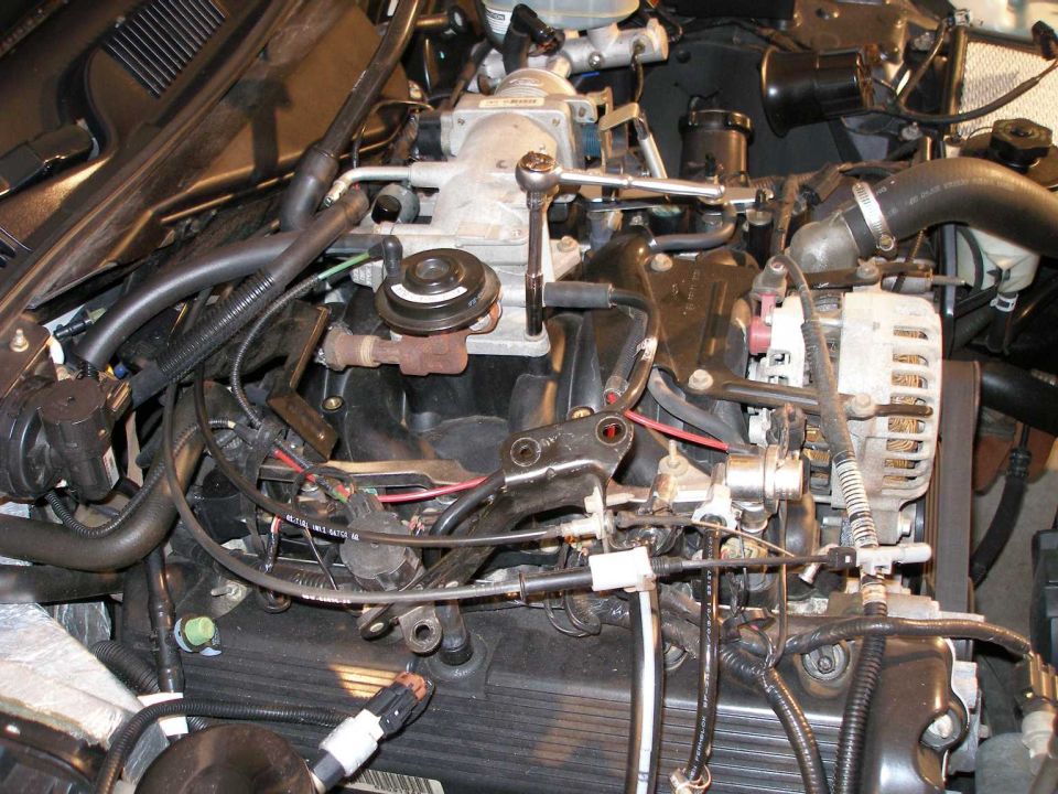 Engine bay close-up with intake manifold, alternator, hoses and wiring during removal work