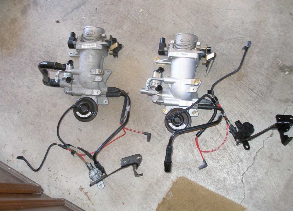 Two automotive throttle bodies with wiring harnesses on a concrete floor