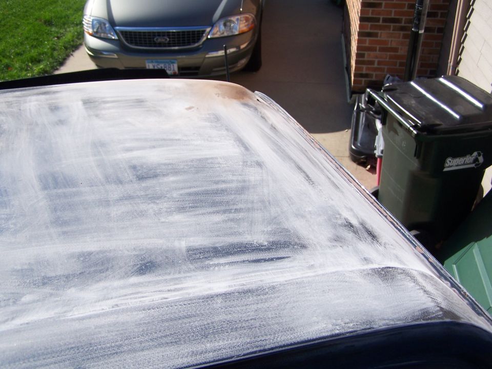 Car roof covered in white compound, with a silver sedan in the background