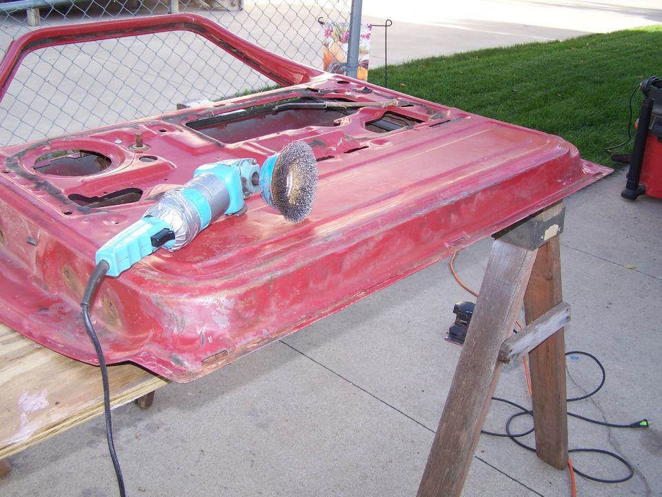 Red car hood on sawhorses being stripped with a wire-wheel angle grinder