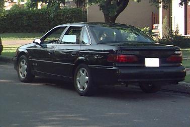 1993 Ford Taurus - A black 1993 Ford Taurus is parked on the side of a street in a residential area.