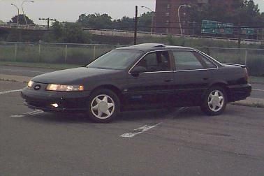 1993 Ford Taurus - A black sedan is parked on a paved surface with painted lines.