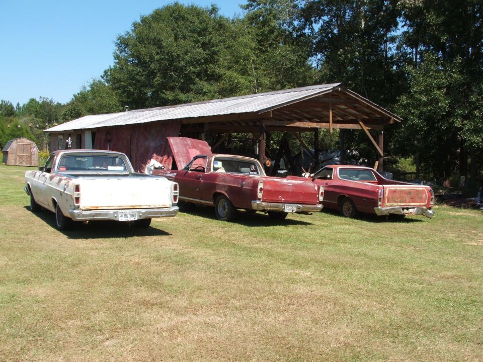 Three Ford Rancheros parked in front of a barn, two red and one white
