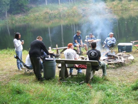 1995 Ford Bronco - A group of people enjoy a campfire gathering by a tranquil lake, with smoke rising into the air.
