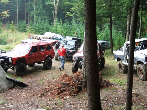 1995 Ford Bronco - A group of off-road vehicles are gathered in a wooded area, with a person walking among them.