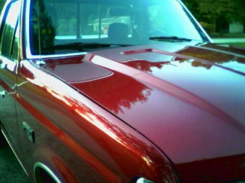 1992 Ford F-150 - Low side angle across the glossy red cowl-induction hood of a pickup, showing the raised center bulge and rear-facing scoop opening near th…