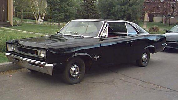 black coupe with chrome bumper and grille, parked on street. another car is behind it