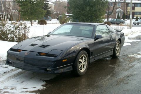 1993 Ford Taurus - This black Pontiac Firebird features pop-up headlights and distinctive hood vents, indicative of a 1985 model year.