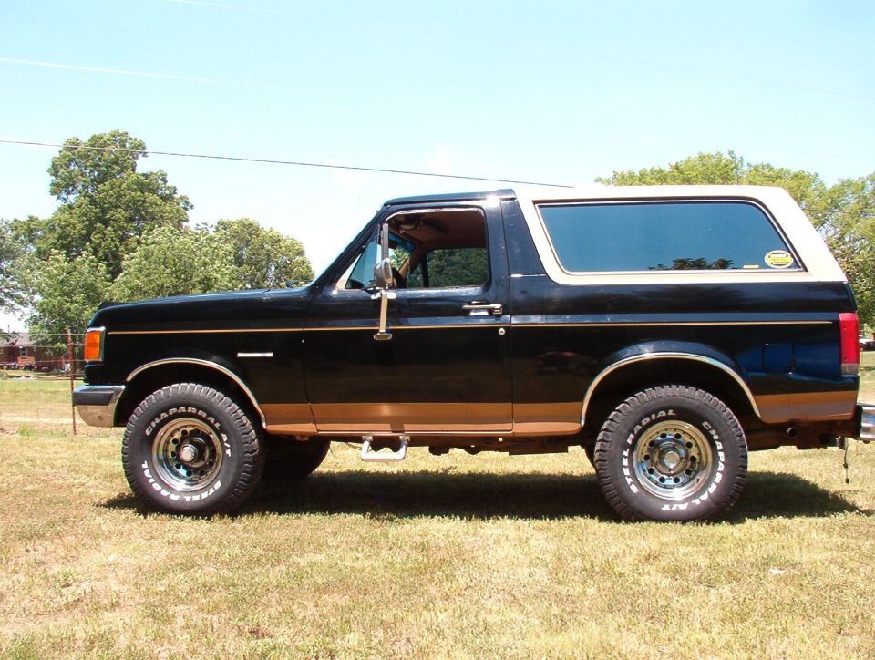 Black 1989 Ford Bronco with tan trim and wheels, parked on grass