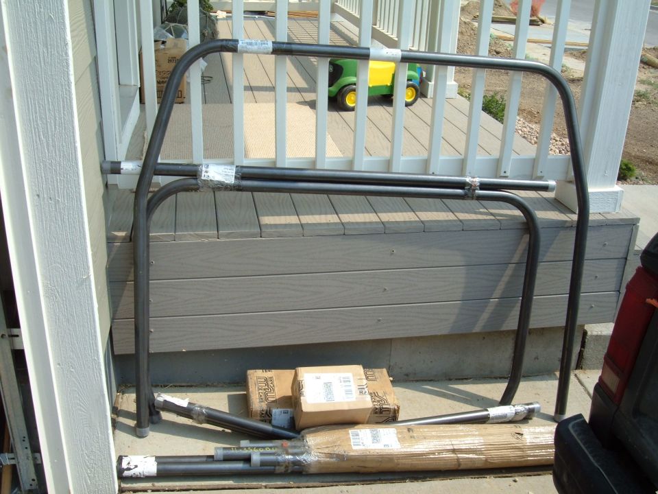Roll cage hoop and loose brace tubes staged against a deck before installation