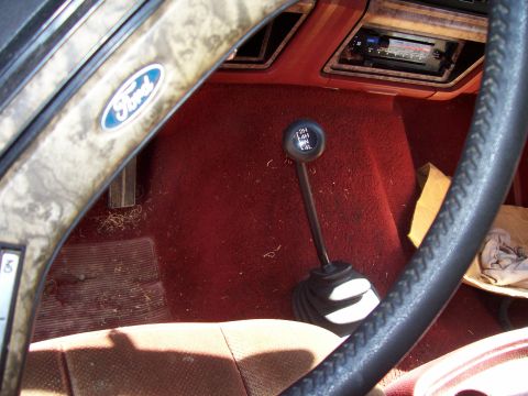 1985 Ford Bronco - The interior of a 1985 Ford Bronco, a four-wheel drive shifter and a classic Ford logo on the steering wheel.