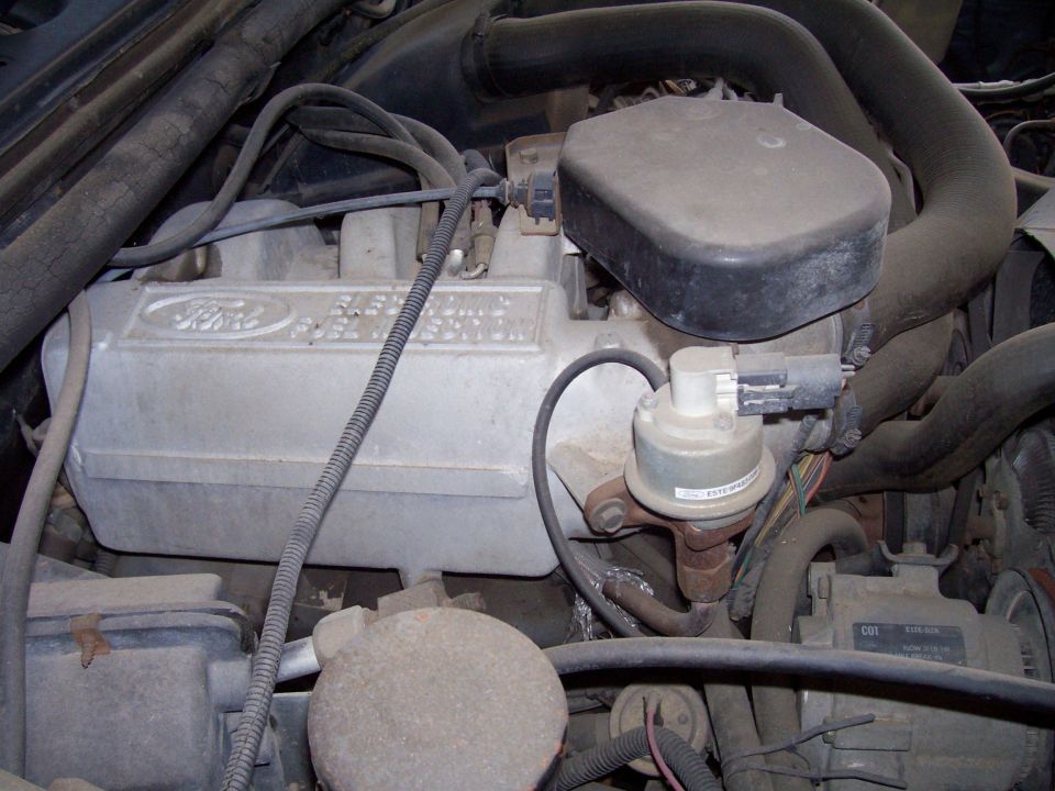 Close-up of a dusty Ford engine with visible valve covers and hoses