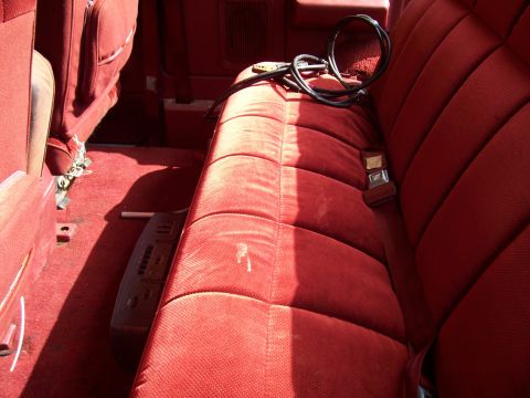1985 Ford Bronco - The interior of a vehicle features red velour seating and carpeting, with a coiled cord and an electronic device visible.