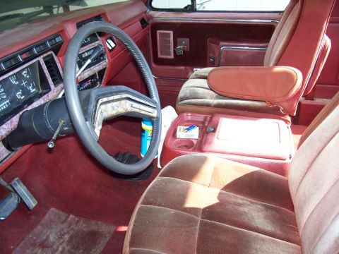 1985 Ford Bronco - The interior of this vehicle features a red dashboard and seats with a brown center console and steering wheel.