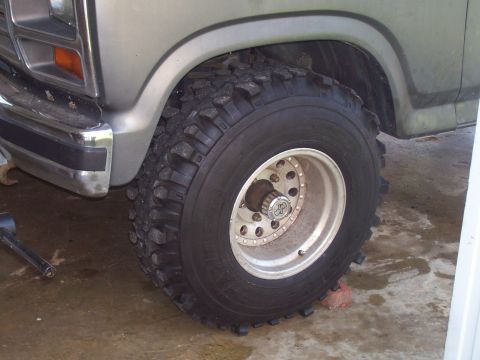 1985 Ford Bronco - A close-up view of a large, aggressive off-road tire mounted on a silver truck's front wheel.
