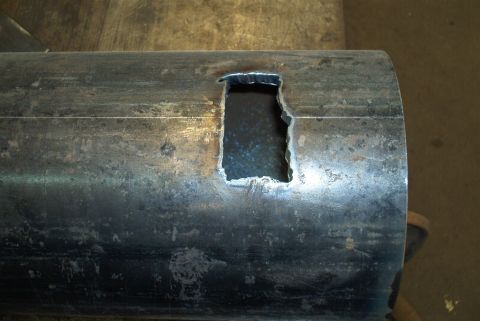 1983 Ford Bronco - A close-up view of a metal pipe with a crudely cut rectangular opening.