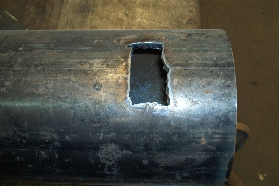 Metal pipe with a rough rectangular cutout, showing weld marks and surface wear