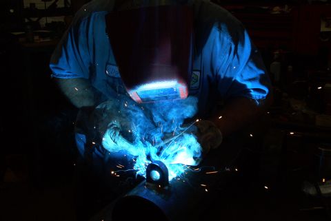1983 Ford Bronco - A welder works on a metal part, creating sparks and smoke.