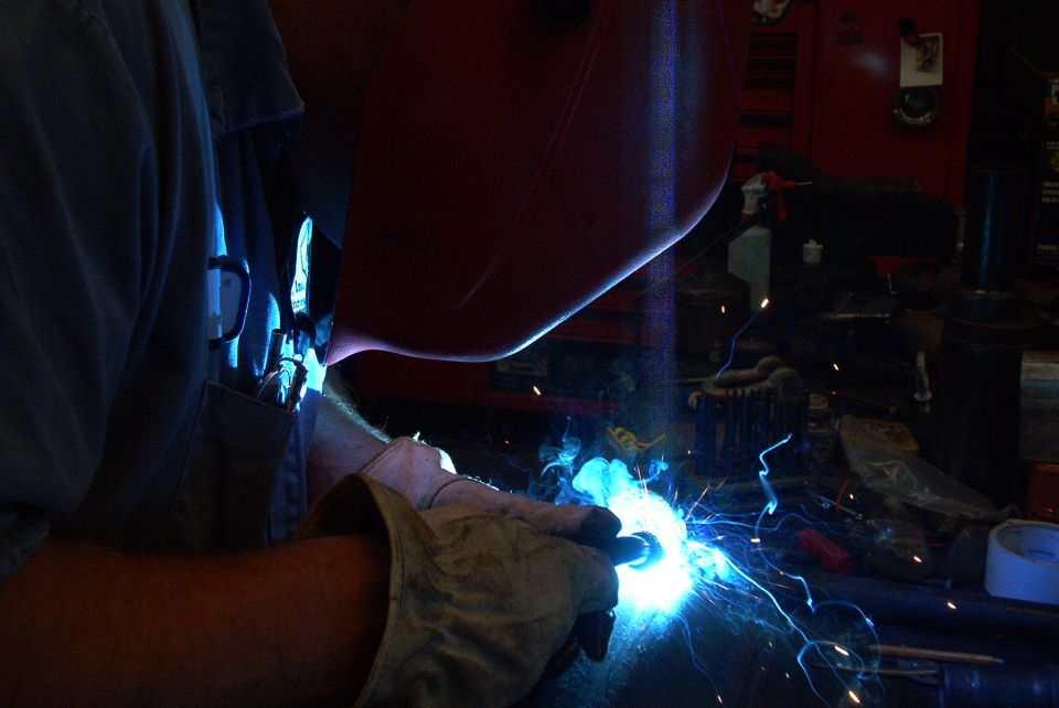 Person welding with bright blue sparks flying. A red welding mask is on