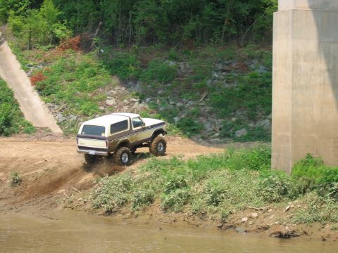 1992 Ford Mustang - Ford Bronco navigating a muddy incline next to a concrete structure and river.